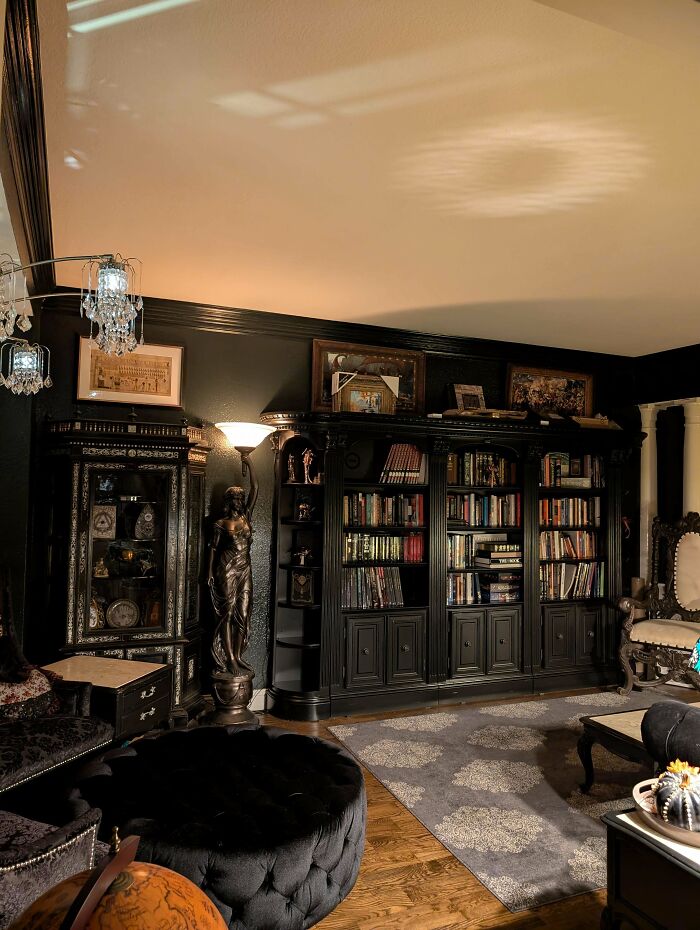 Dark vintage living room with ornate bookshelves, decorative statues, and eclectic decor embracing more is more home style.