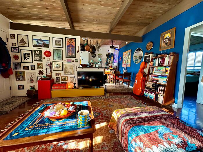 Cozy living room displaying a more is more home decor style with colorful textiles, wall art, books, and eclectic furnishings.
