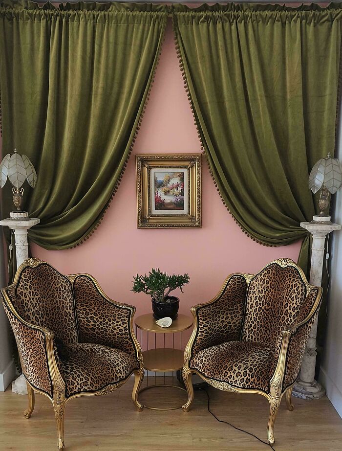 Two ornate leopard print armchairs with gold frames in a home decorated with green velvet curtains and a small framed painting