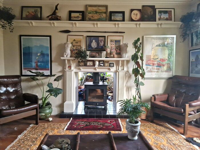 Cozy living room richly decorated with framed art, plants, and vintage furniture embracing more is more home decor style.