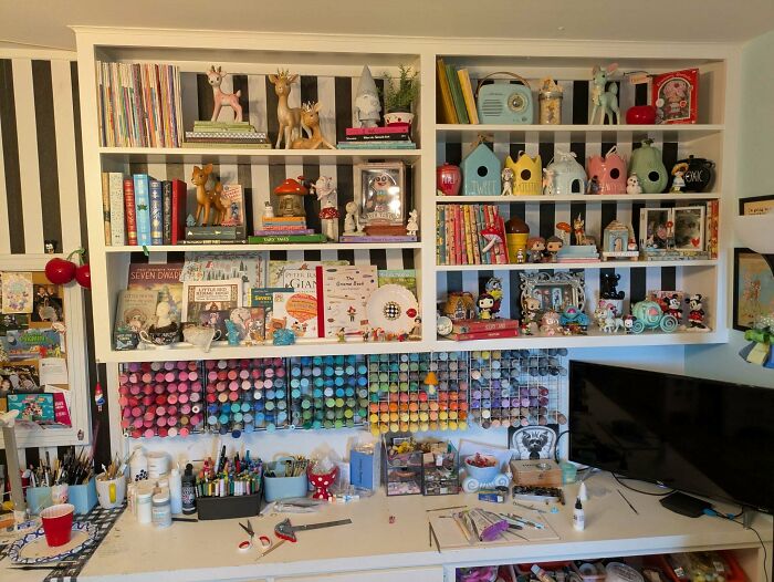 Colorful craft supplies and eclectic decor filling shelves and workspace in a more is more home interior design.