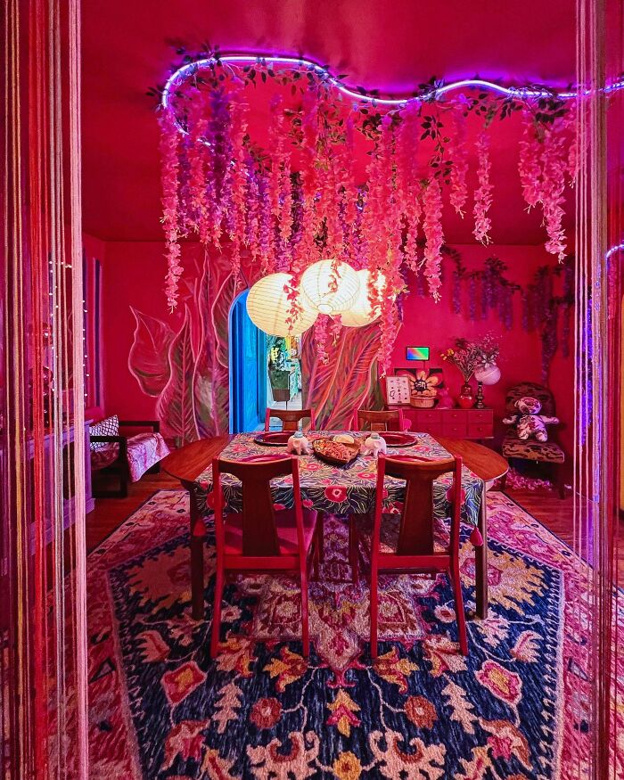 Vibrant dining room decked out with floral patterns, hanging flowers, and colorful lighting showcasing more is more home decor.