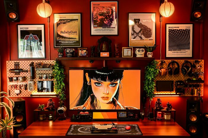 Eclectic home office setup with vibrant art, hanging plants, tech gadgets, and framed posters embracing more is more decor style.