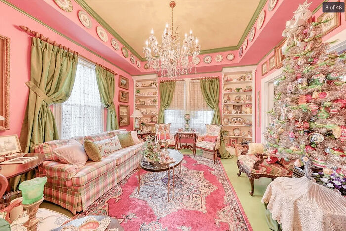 Living room with vibrant decor, patterned sofa, ornate chandelier, and a heavily decorated Christmas tree showcasing more is more home style.