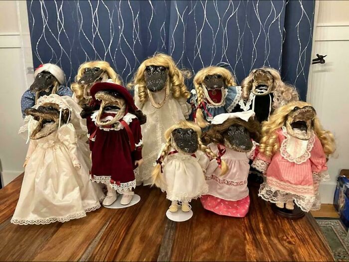 A collection of cursed DIY dolls dressed in vintage clothes with wigs, displayed on a wooden table indoors.