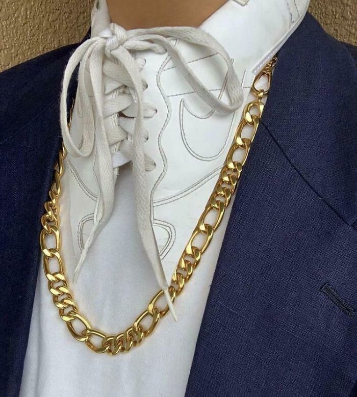 White sneaker used as a necklace pendant, tied with shoelaces, worn with a gold chain and blue blazer in a cursed DIY project.