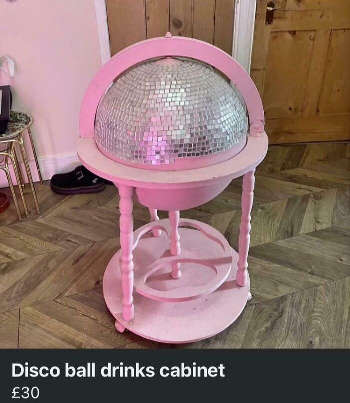 Pink DIY disco ball drinks cabinet with mirrored globe top in a wooden room with parquet flooring.
