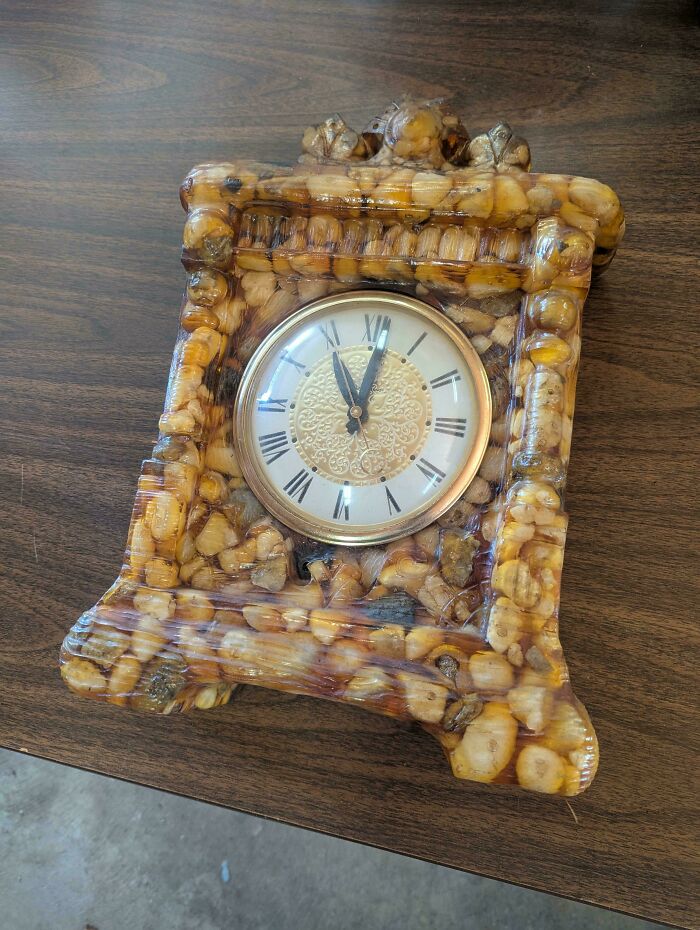 Clock with a bulky DIY resin frame filled with random objects, showcasing a deeply cursed DIY project on a wooden surface.
