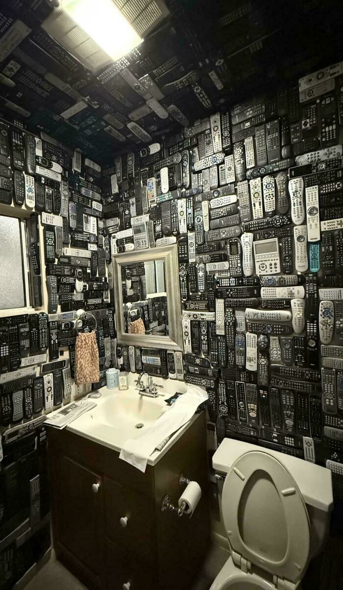 Bathroom walls and ceiling covered with hundreds of remote controls in a deeply cursed DIY project.