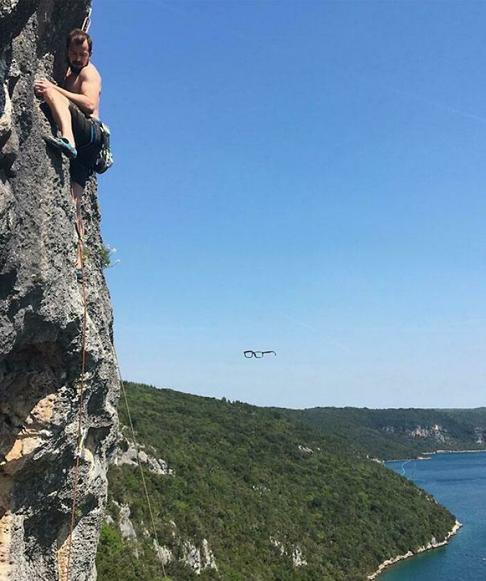 Man rock climbing on a cliff with a pair of glasses appearing to float in midair in the unexpected photo.