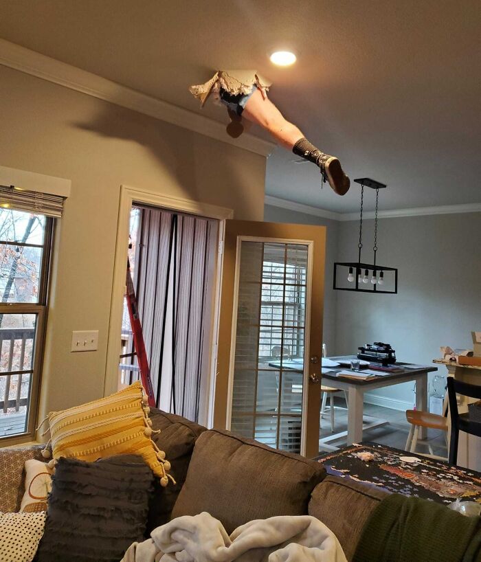 Legs sticking through ceiling hole above couch in living room, a funny photo that says it all instantly.
