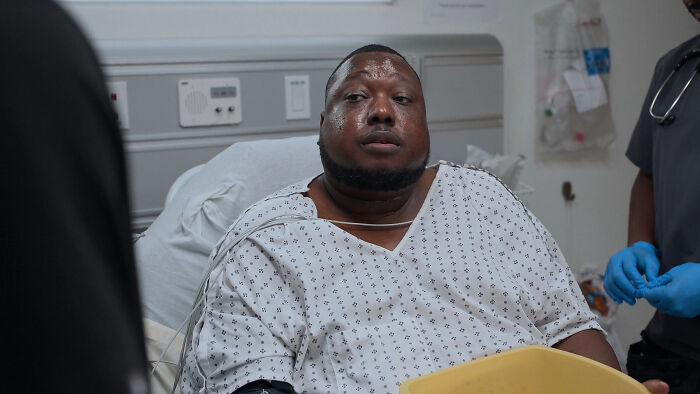 Guest cast member from The Pitt Season 2 Episode 6 wearing hospital gown in a medical setting with staff nearby. - 7