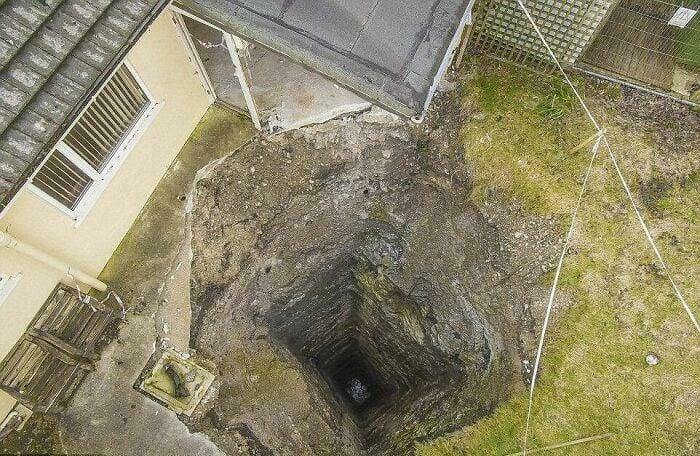 Aerial view of a deep, square hole in the ground next to a house and grassy yard, a creepy image.