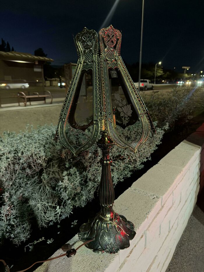 An ornate vintage metal lamp with intricate designs, a jackpot find from a thrift store displayed outdoors at night.