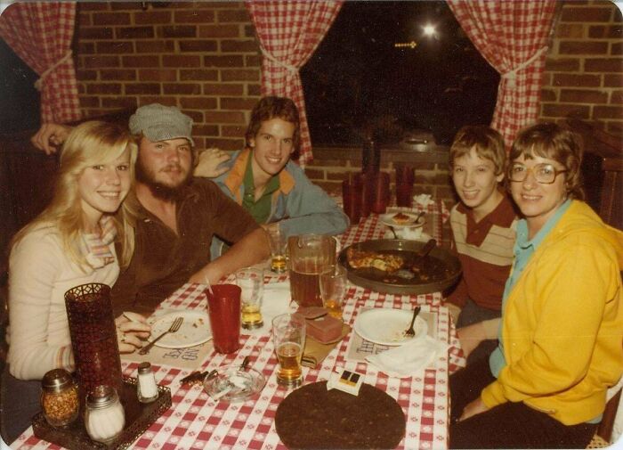 A group of five friends gathered around a checkered table at a restaurant, a candid old photo from generations ago.