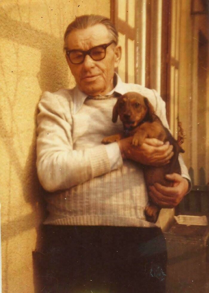 An older man wearing glasses holds a small dachshund puppy in this candid old photo from generations ago.