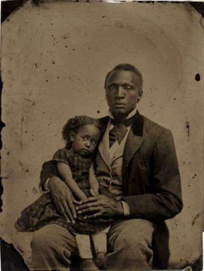 Victorian era photo of a man in formal attire holding a young girl, showcasing period clothing and family portrait style.