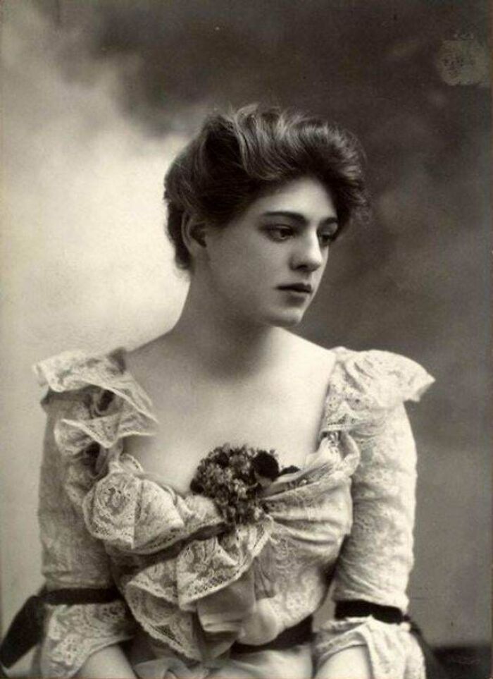Victorian era photo of a woman in lace dress with floral embellishment, reflecting the period's fashion and style.