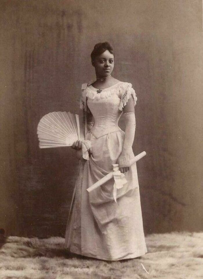 Victorian Era photo of a woman in period dress holding a fan and scroll, showcasing fashion and style from the era.