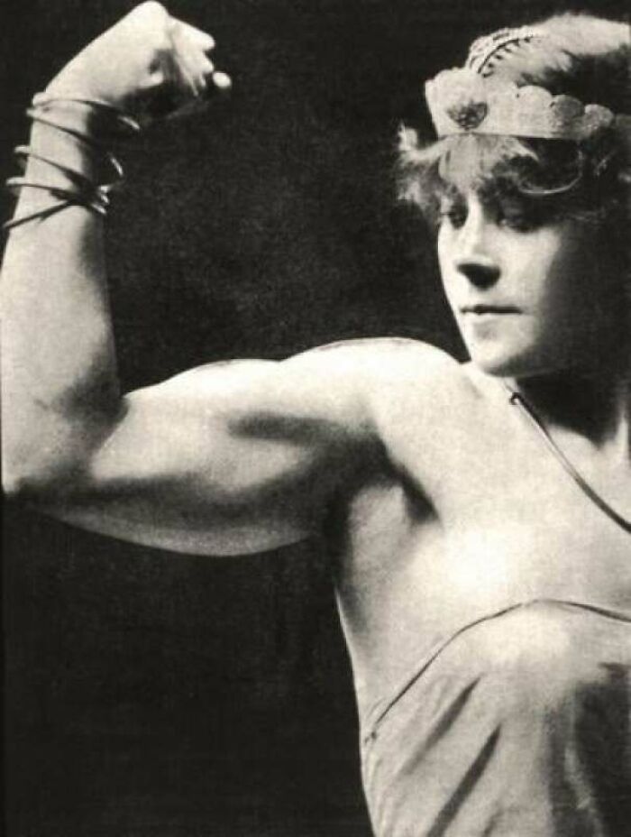 Victorian era photo of a woman flexing her arm muscle, showcasing strength and unique perspectives of the period.