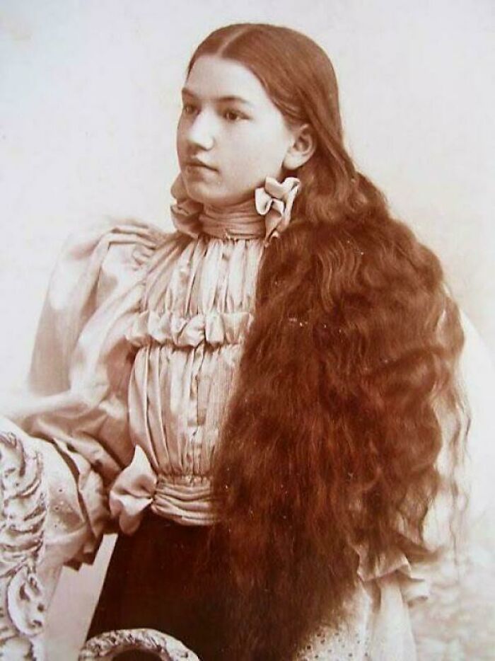 Victorian era photo of a young woman with long flowing hair wearing a high-necked Victorian dress and bow accessories.