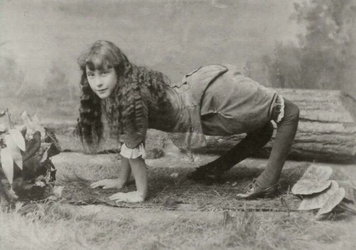 Young woman performing a gymnastic pose outdoors in a vintage Victorian Era photo with period attire and setting.