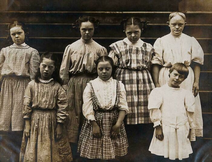 Group of Victorian Era children with Down syndrome wearing period dresses posing for a photo on wooden steps