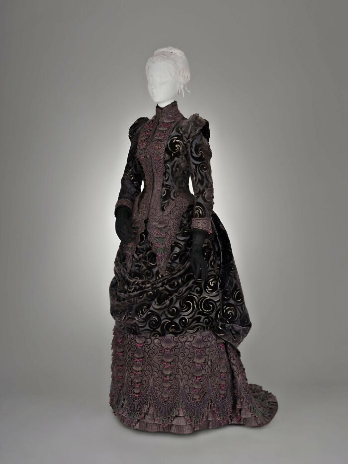 Victorian era dress with intricate black and purple patterns displayed on a mannequin in a studio setting.