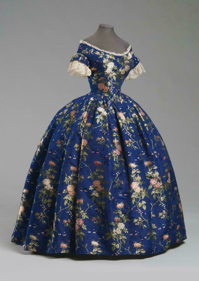 Victorian era floral dress with off-shoulder lace sleeves and full skirt showcasing period fashion details.