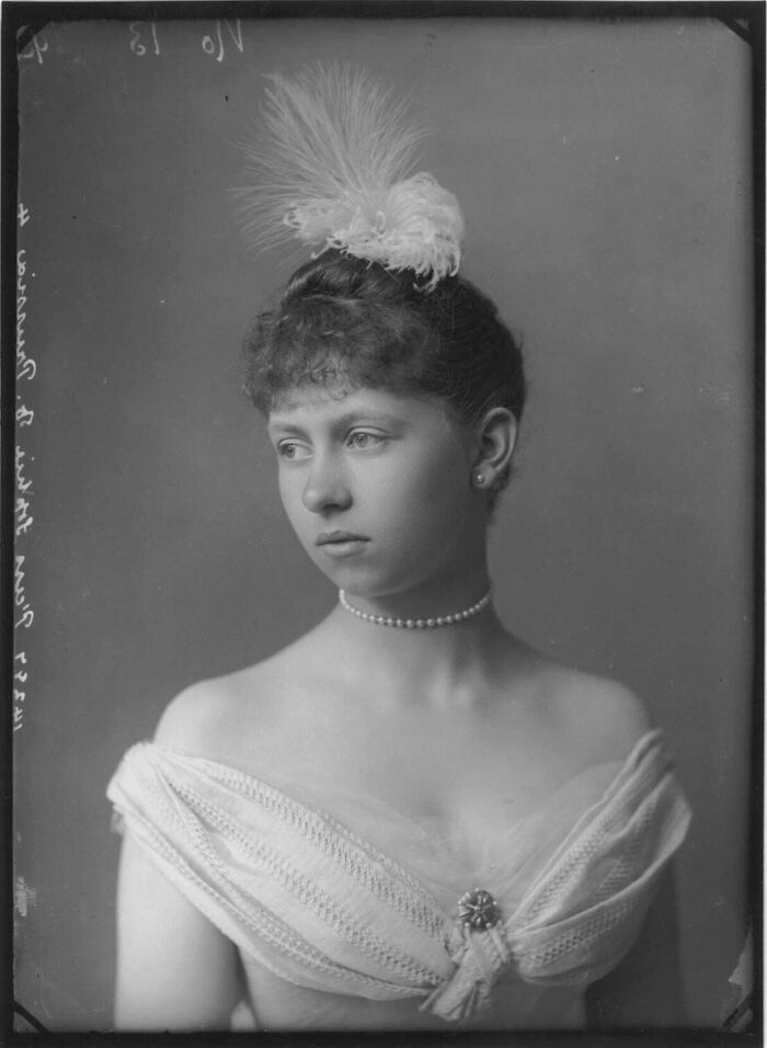 Victorian era portrait of a young woman wearing a pearl necklace and feathered headpiece, showcasing period fashion and style.