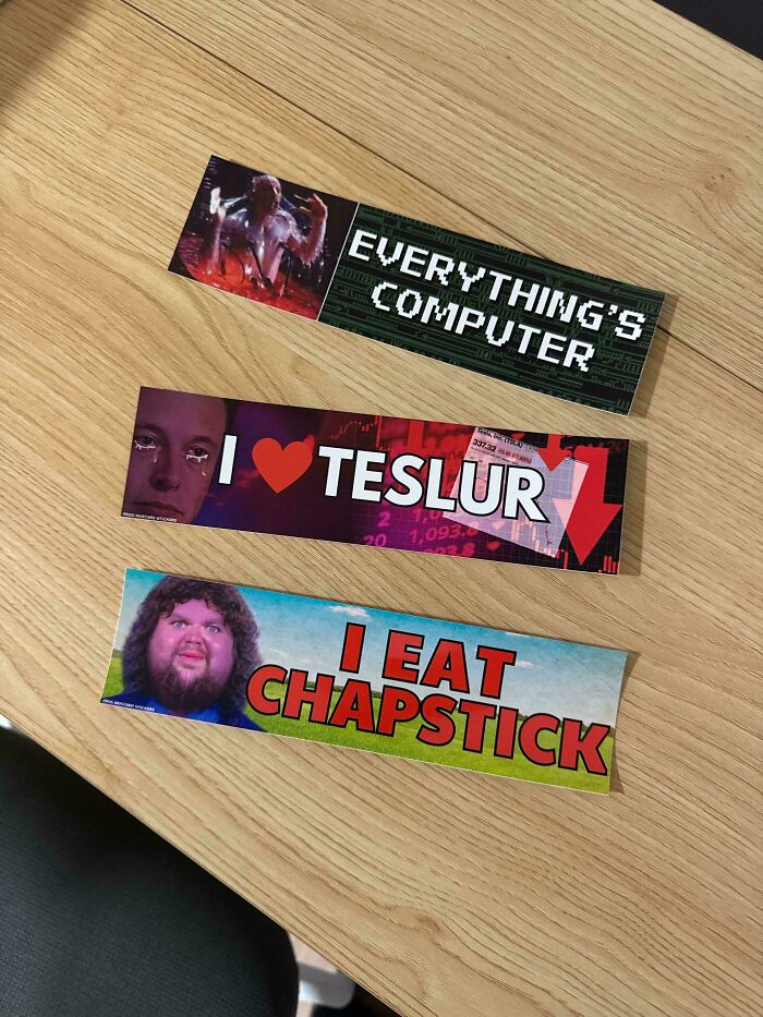 Three colorful bumper stickers with humorous and tech-related phrases on a wooden table