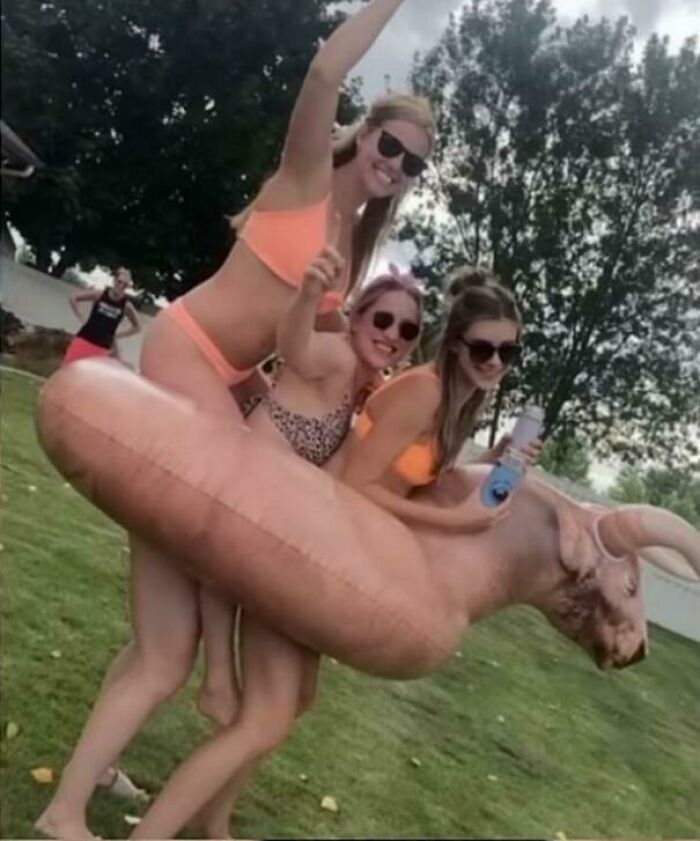 Three women in bright swimwear pose with a bull-shaped float in a misleading and confusing photo that looks like a real-life glitch.