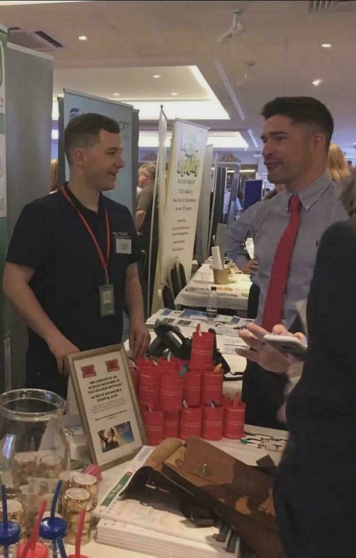 Two men talking at a crowded event with red cans and informational displays creating a misleading photo glitch effect.