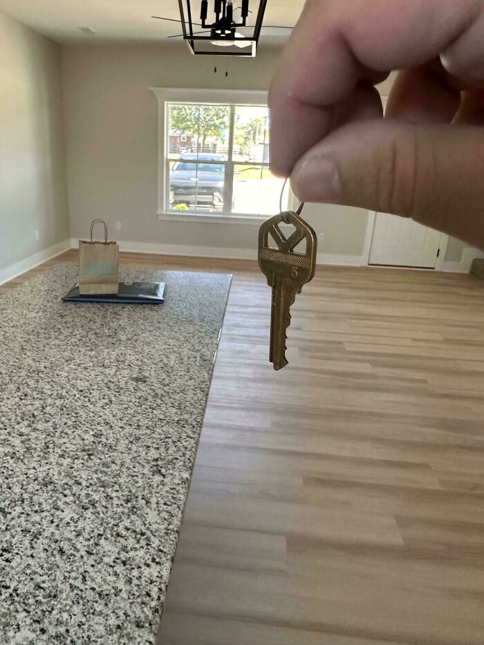 Hand holding a key in an empty room with a marble countertop and wooden floor creating a misleading photo illusion.