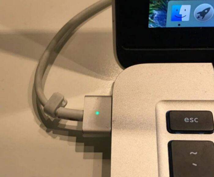 Close-up of a laptop with a charging cable glowing green, creating a misleading and confusing photo effect.