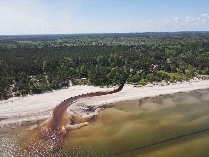 Aerial view of a beach where a river of dark water flows into the sea, creating a misleading and confusing natural photo.