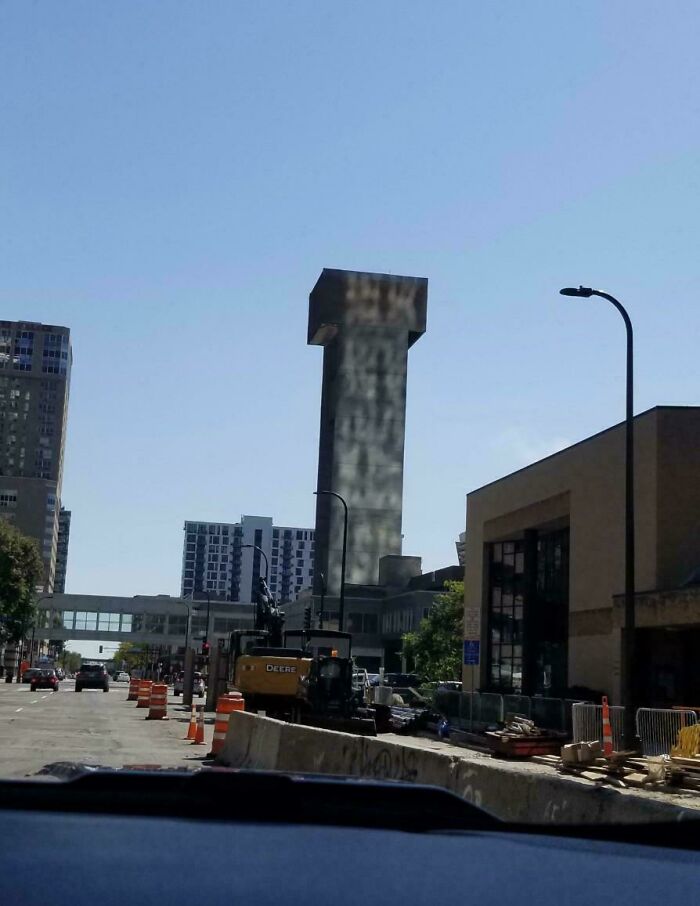 Tall building with unusual reflection appears like a glitch, surrounded by urban construction and cityscape under clear sky