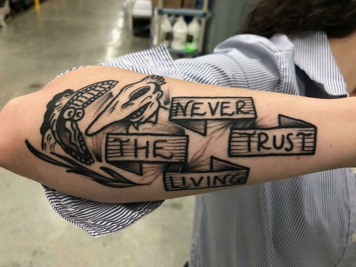 Tattoo of a banana, hand, and arrows with the comedic sign that went wrong saying never trust the living.