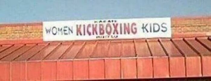 Sign with the words women kickboxing kids, showing a comedic fail with misplaced spacing in outdoor setting.