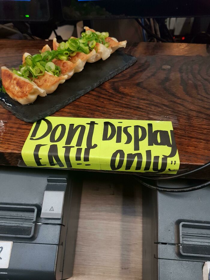 Plate of dumplings with green garnish on a wooden counter displaying a funny sign that went wrong into comedic gold.