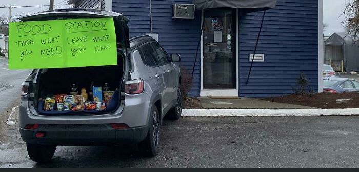 Car trunk open with food station sign saying take what you need, leave what you can, a comedic sign fail outdoors.