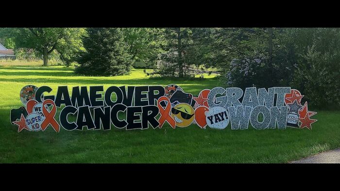 Large yard sign with the comedic gold of a cancer victory message reading game over cancer grant won with emojis and ribbons.