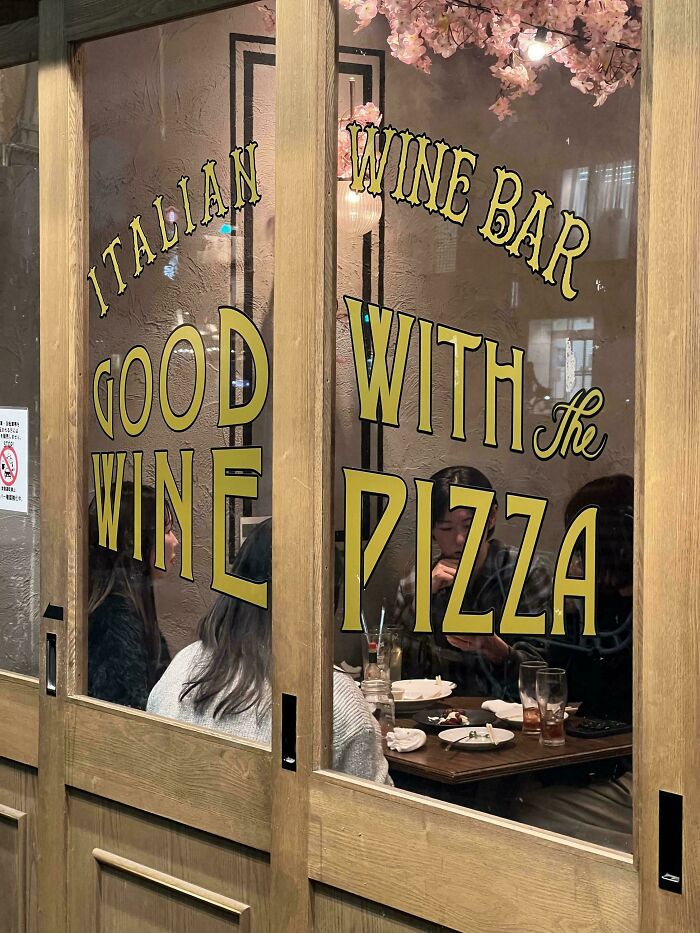 Italian wine bar sign with text good wine with the pizza seen through wooden framed glass door, comedic signage fail.