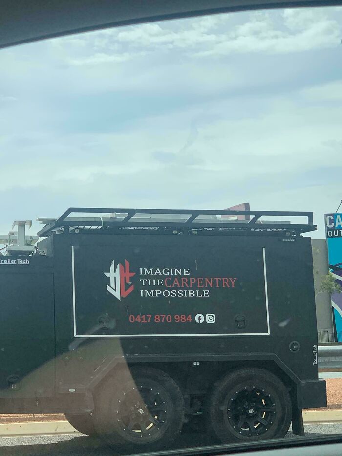 Black vehicle with a humorous carpentry sign showing text that went wrong, highlighting comedic gold in signage fails.