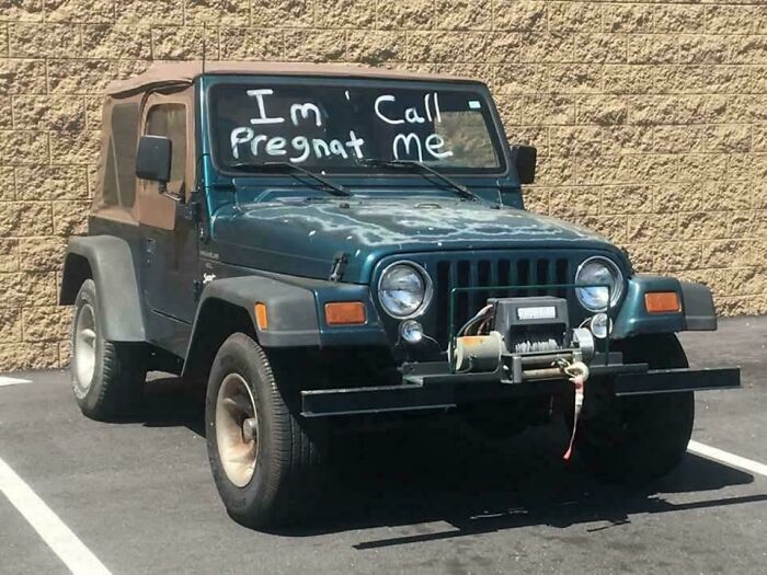 Old Jeep with a humorous sign on the windshield showing a comedic sign that went wrong, parked outdoors.
