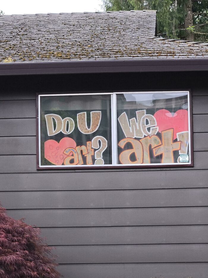 Comedic sign in window asking do you art we art with large colorful letters and heart shapes displayed on house wall.