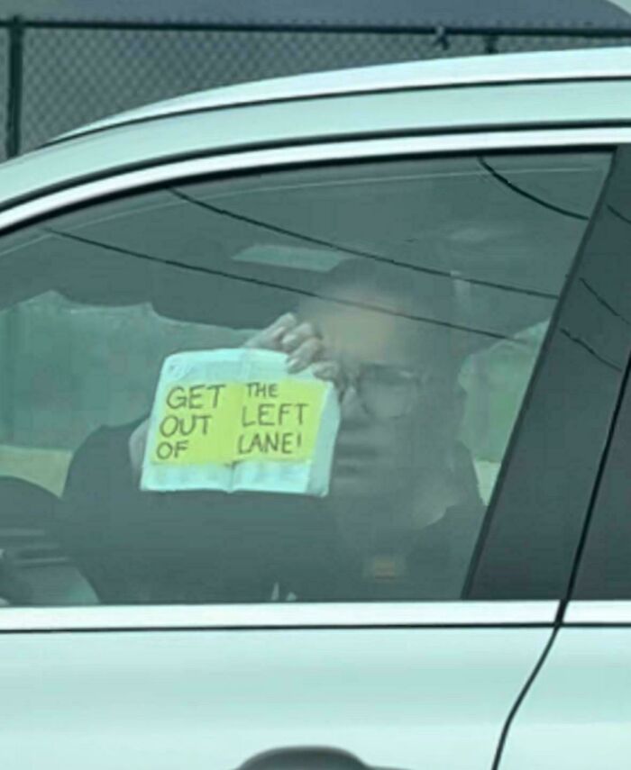 Man inside car holding a handwritten sign saying get out of the left lane, a comedic sign that went wrong.