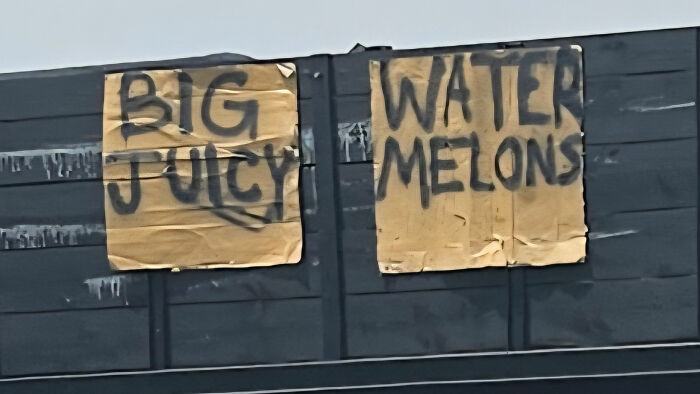 Handwritten cardboard signs reading big juicy and water melons, a comedic sign fail turning into comedic gold.