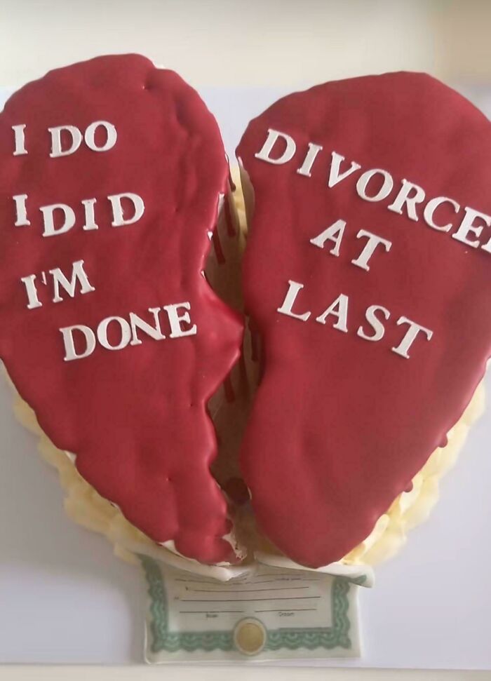 Broken red heart-shaped cake with white letters displaying a comedic sign that went wrong about divorce and being done.
