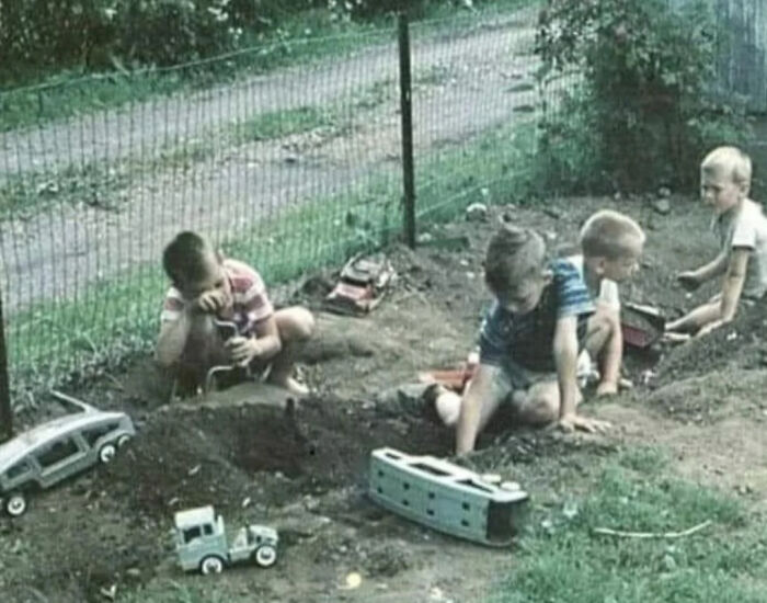 Four young children playing in dirt with toy trucks and cars, a nostalgic image that takes you way back to simpler times.